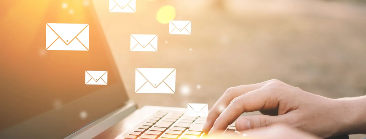 Hands typing on laptop with small email envelope icons floating above