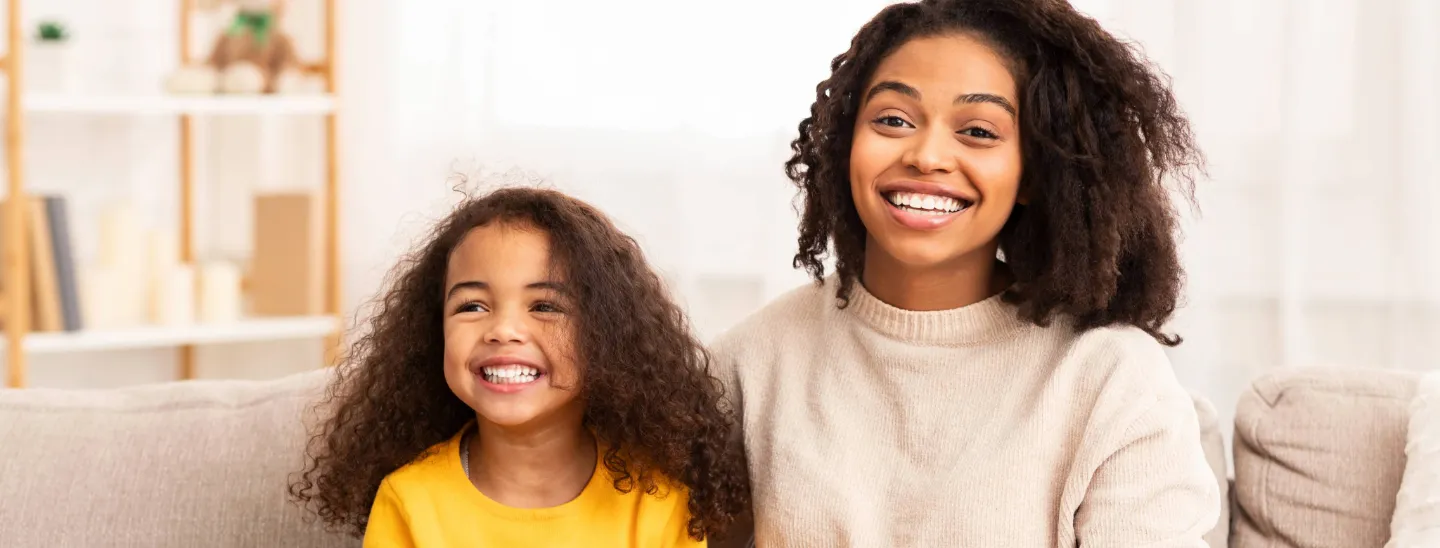Young woman and girl smile on couch holding piggy bank